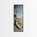 Framed Canvas Print Skinny Art of a Weathered Driftwood Tree Trunk on a Sandy Shore with a Calm Ocean Backdrop, Ideal Tall Art for Coastal Decor